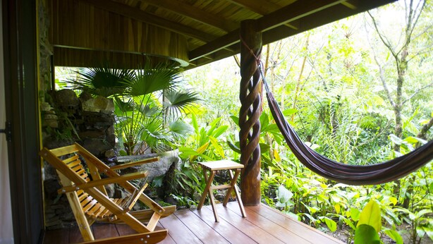 A wooden deck with a hammock, rocking chairs, and a small table. - Hotel Catarata Río Celeste (Katira)
