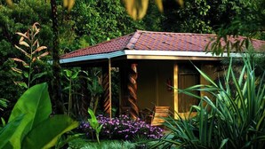 A small, rustic building with a tiled roof, surrounded by lush greenery and flowering plants. - Hotel Catarata Río Celeste (Katira)