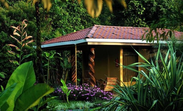 A small, rustic building with a tiled roof, surrounded by lush greenery and flowering plants. - Hotel Catarata Río Celeste (Katira)