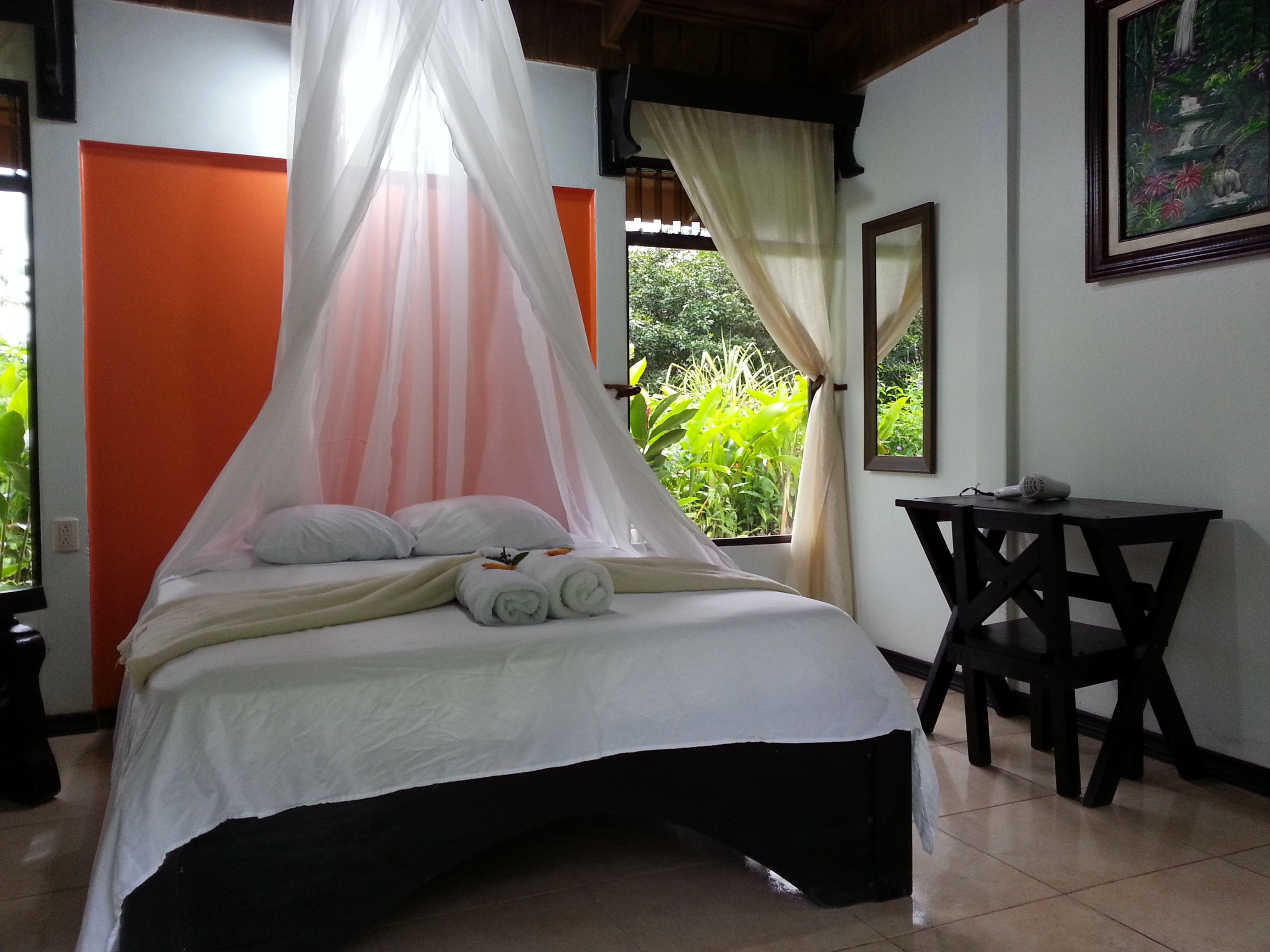 A bed with a canopy, a desk, and a chair in a room with a view of greenery.