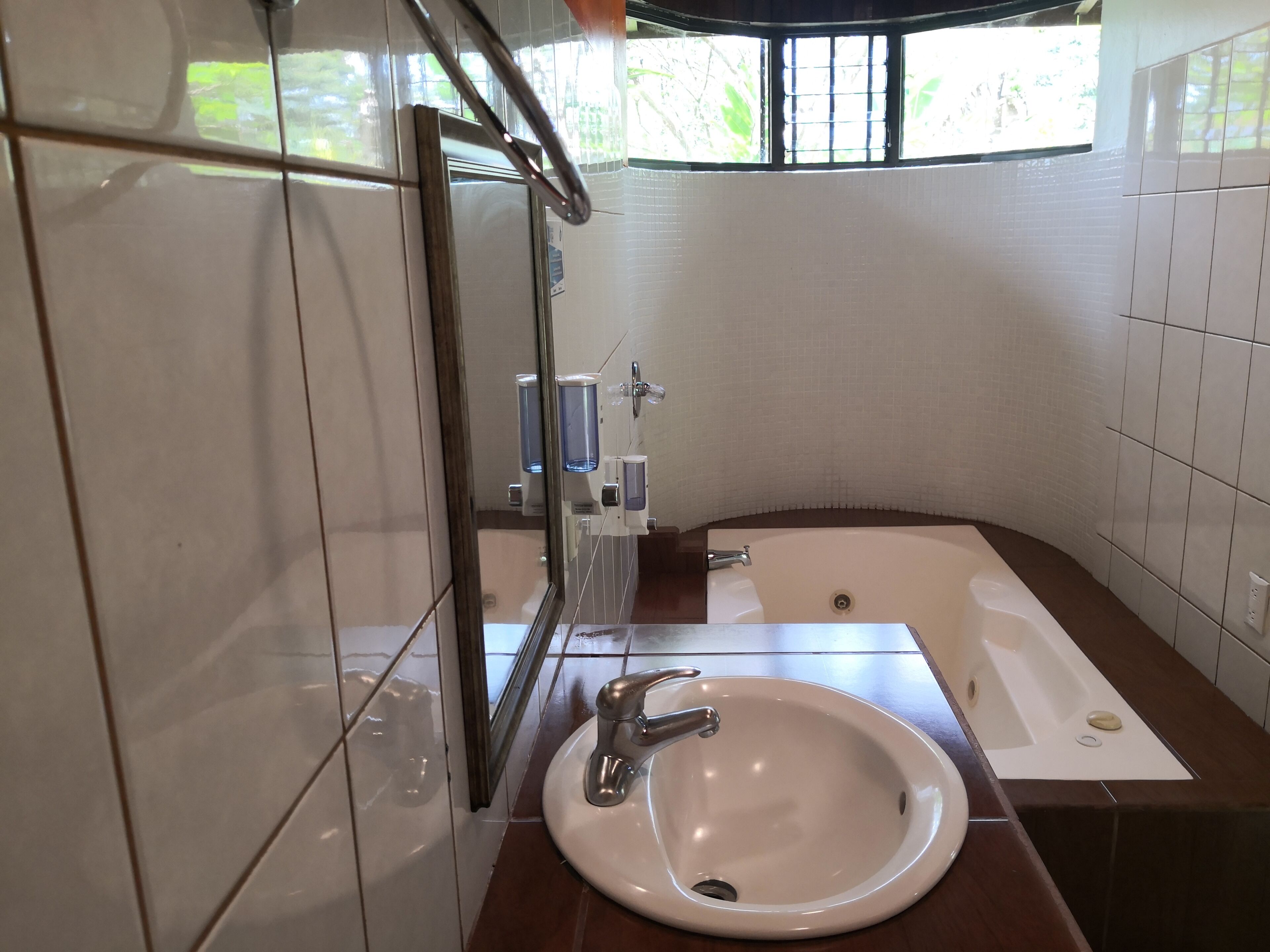 A bathroom with a white sink, a mirror, a bathtub, and a window with bars.