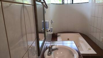 A bathroom with a white sink, a mirror, a bathtub, and a window with bars.