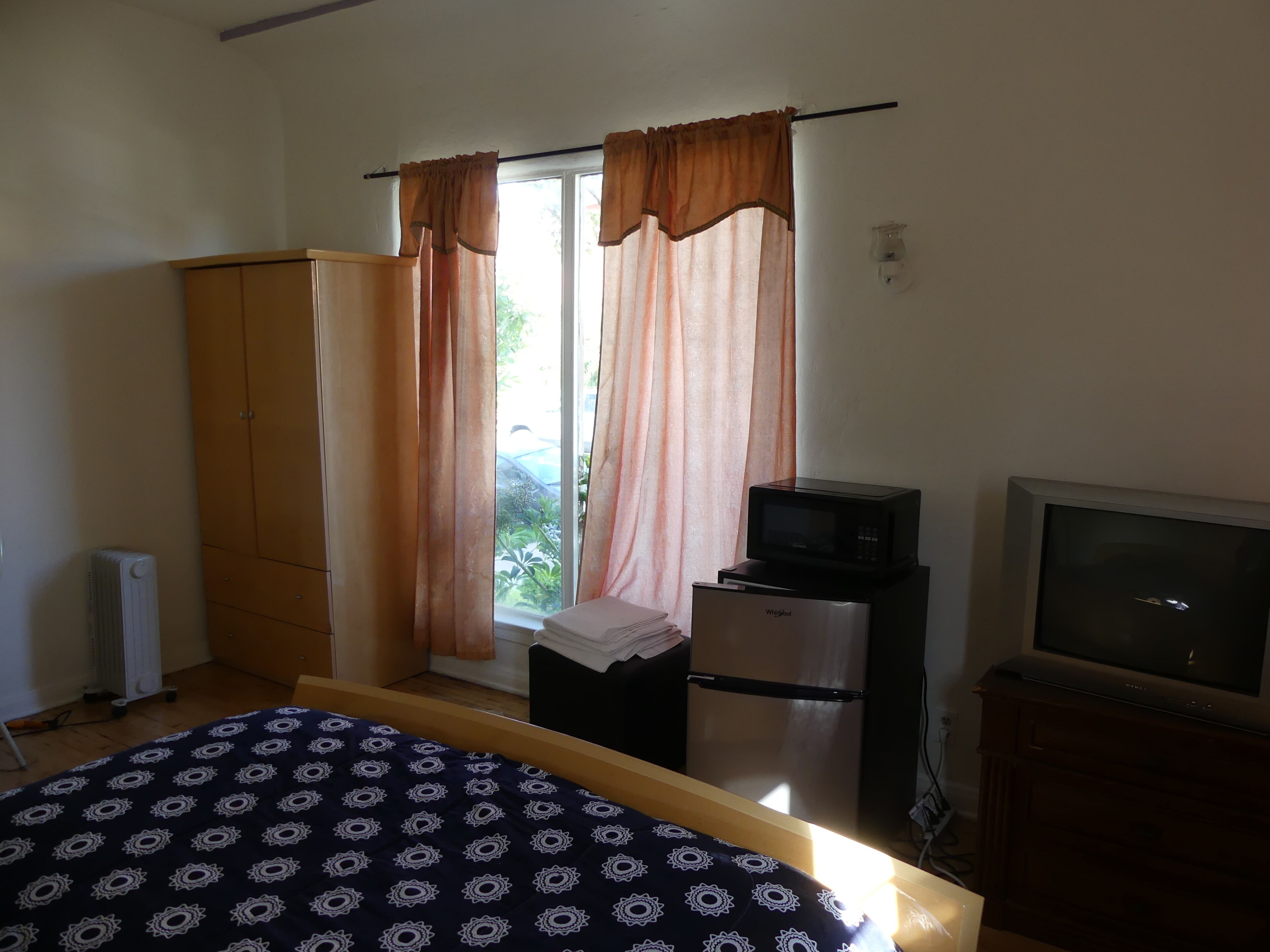Une chambre à coucher comprenant un lit, une télévision, un réfrigérateur et une fenêtre avec des rideaux.