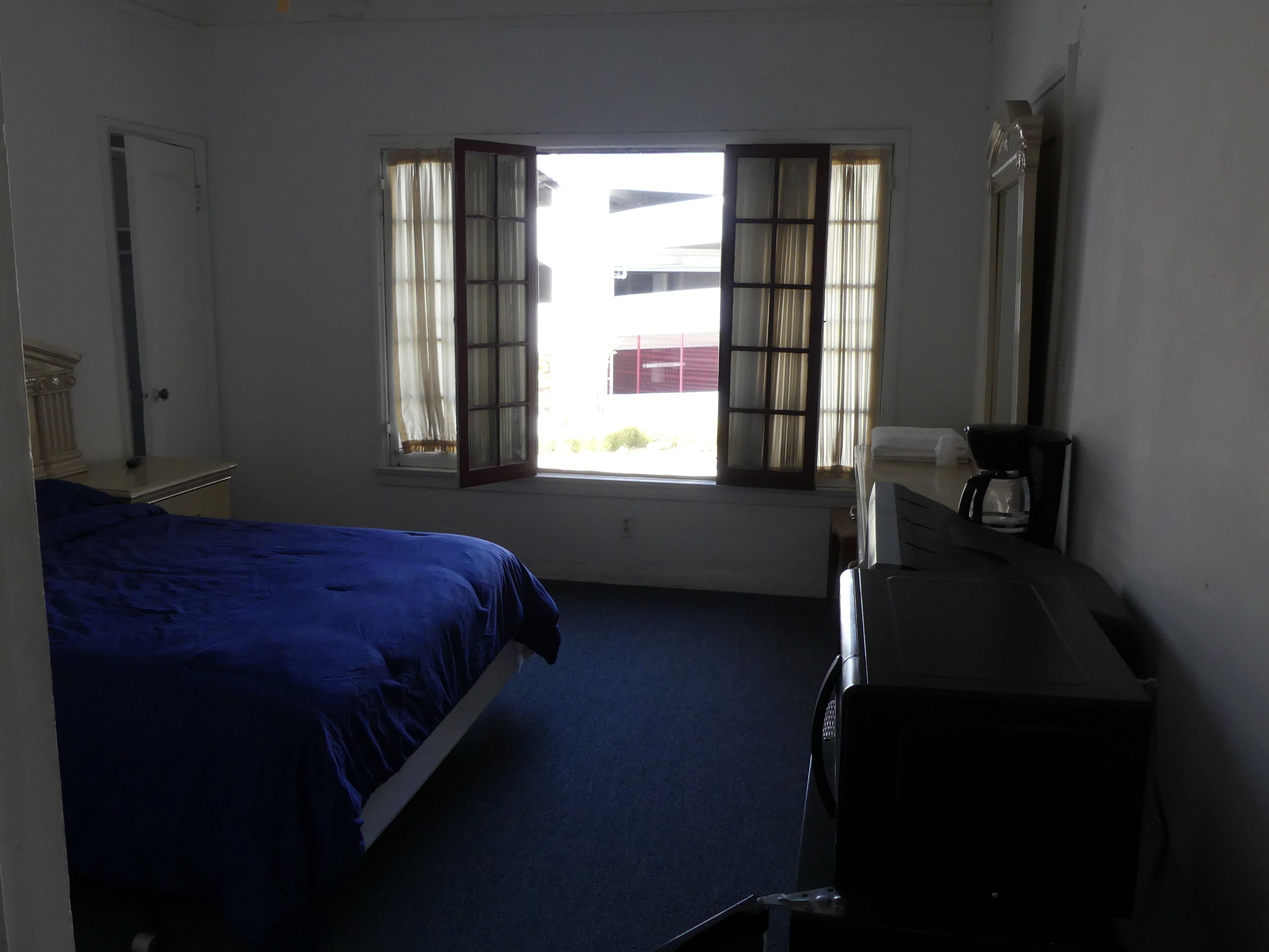 A hotel room with a bed, a desk, a coffee maker, and a window with curtains.
