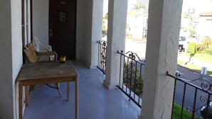 Un balcon avec une table et des chaises en bois, une porte portant l’inscription « B03 », et une vue sur la rue et la verdure.