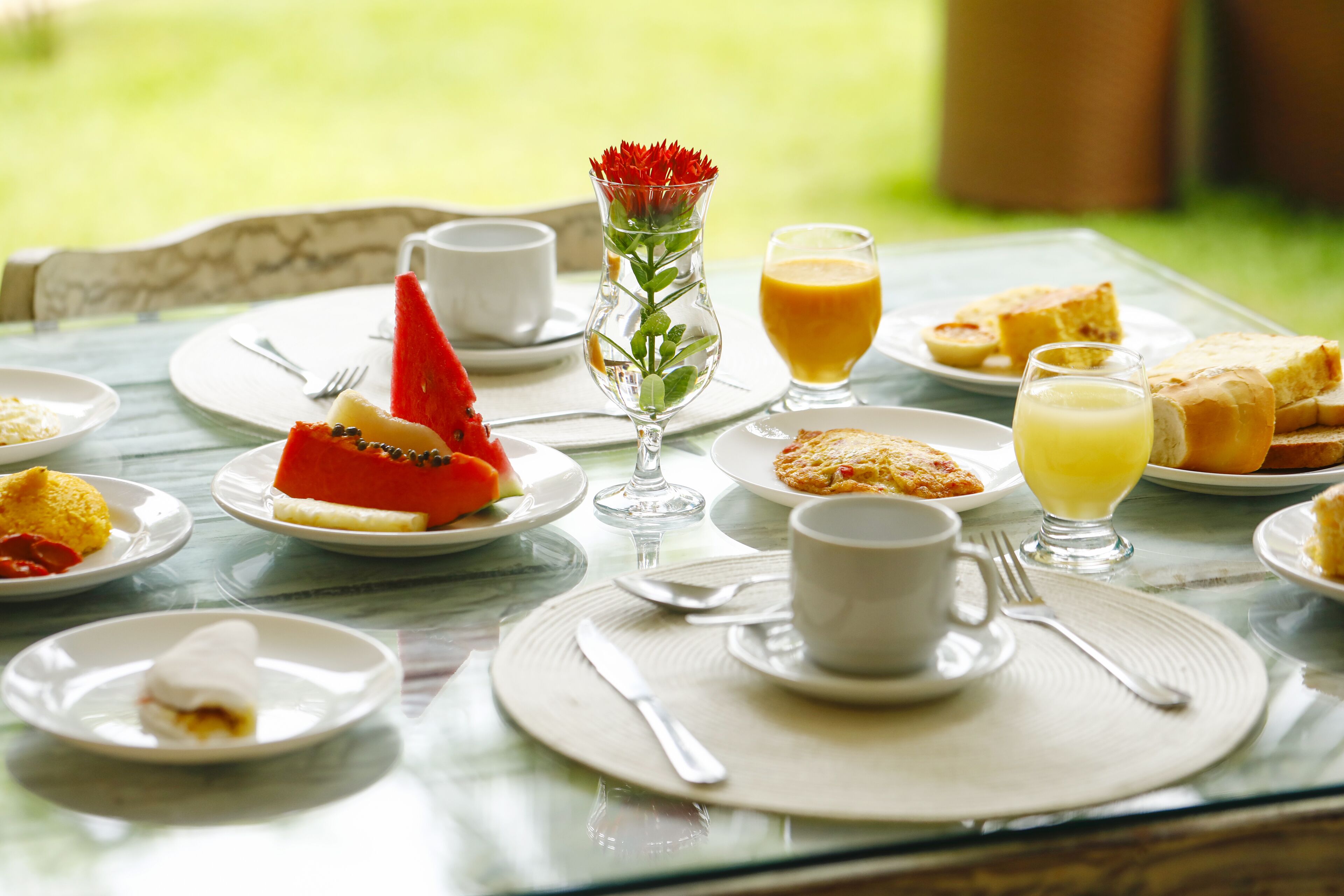 Una mesa de desayuno con platos de comida, un florero con flores y un vaso de jugo de naranja.