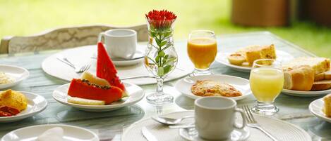 Una mesa de desayuno con platos de comida, un florero con flores y un vaso de jugo de naranja.