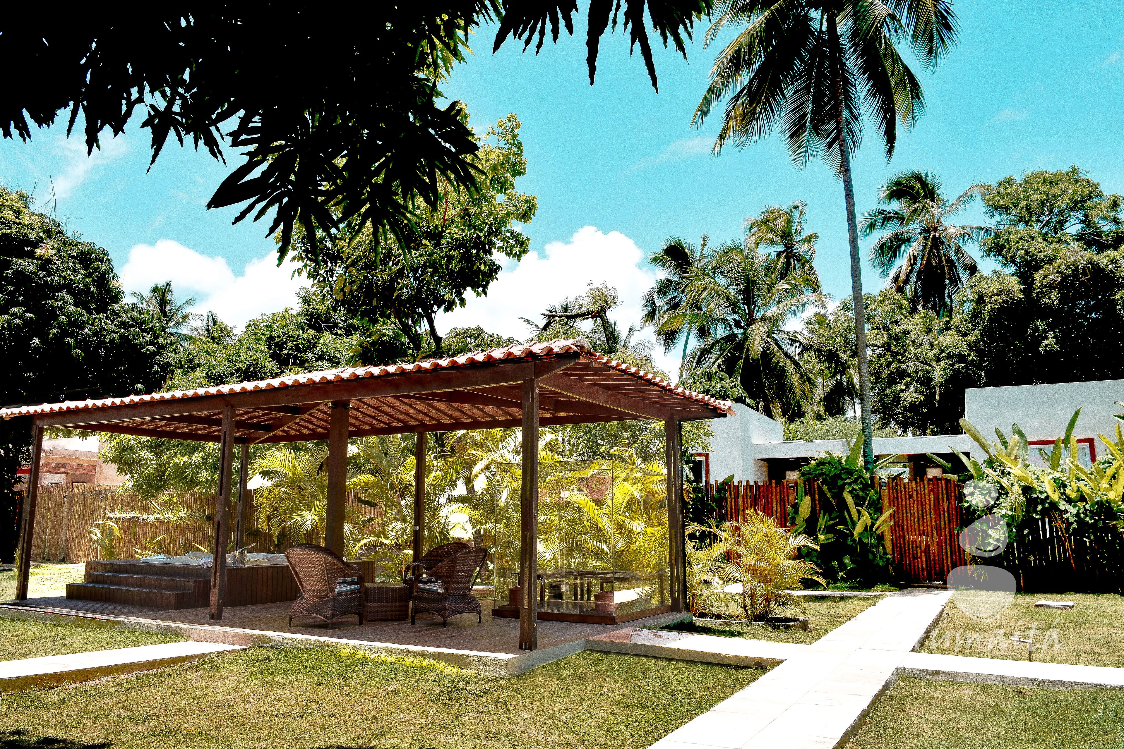 A covered outdoor seating area with a hot tub, surrounded by lush greenery and palm trees.