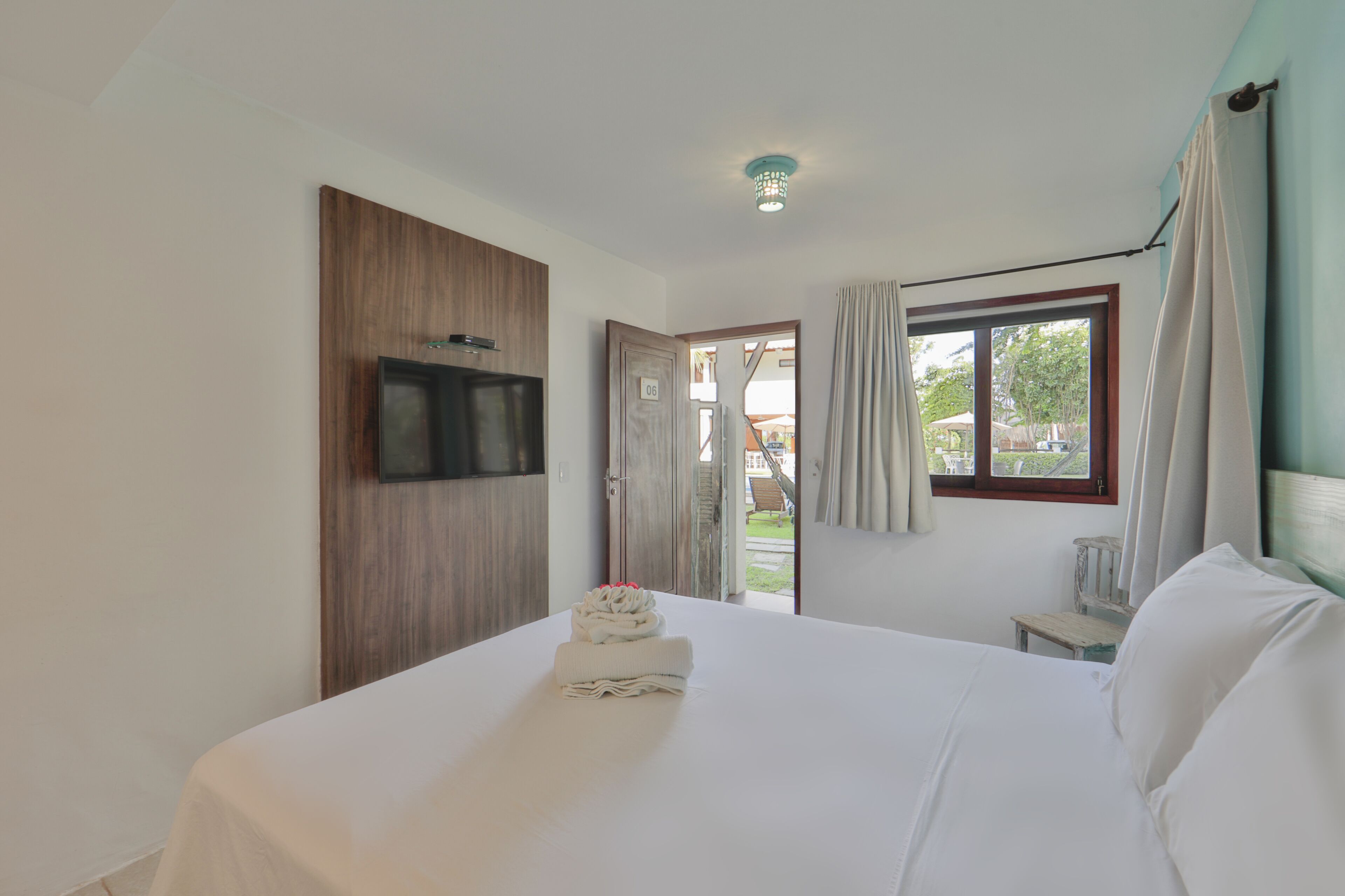 A hotel room with a bed, a TV mounted on the wall, a window with curtains, and a door leading outside.