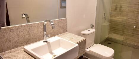 A modern bathroom with a granite countertop sink, a toilet, and a glass-enclosed shower.