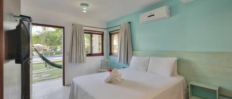 Habitación de hotel con cama, televisor, ventana con cortinas, unidad de aire acondicionado y vistas al exterior.