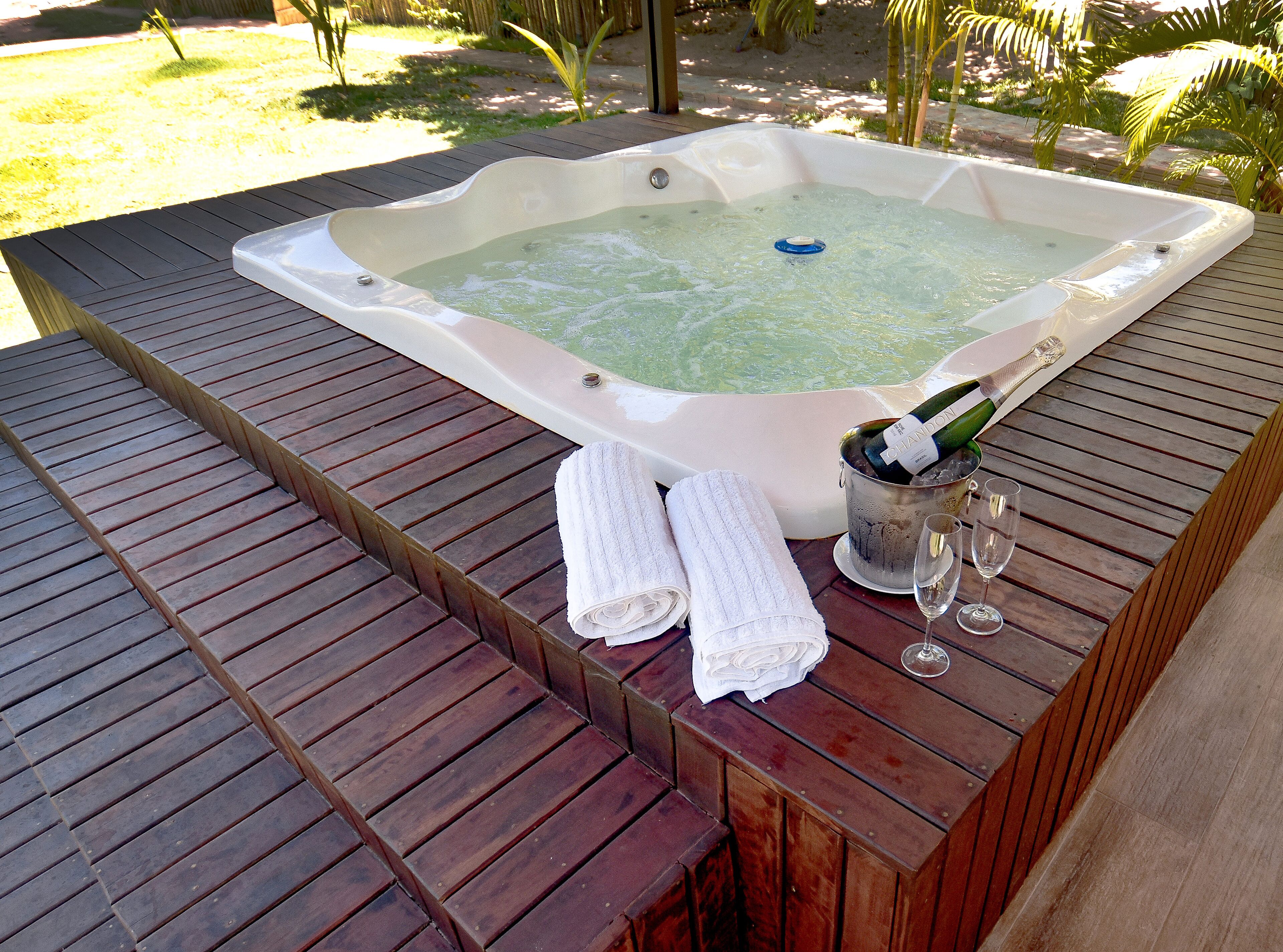 A hot tub with a champagne bottle and glasses on a wooden deck.