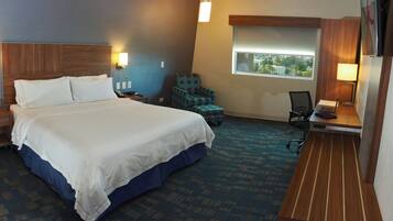 A hotel room with a large bed, a desk with a laptop, a chair, and a window with a view.