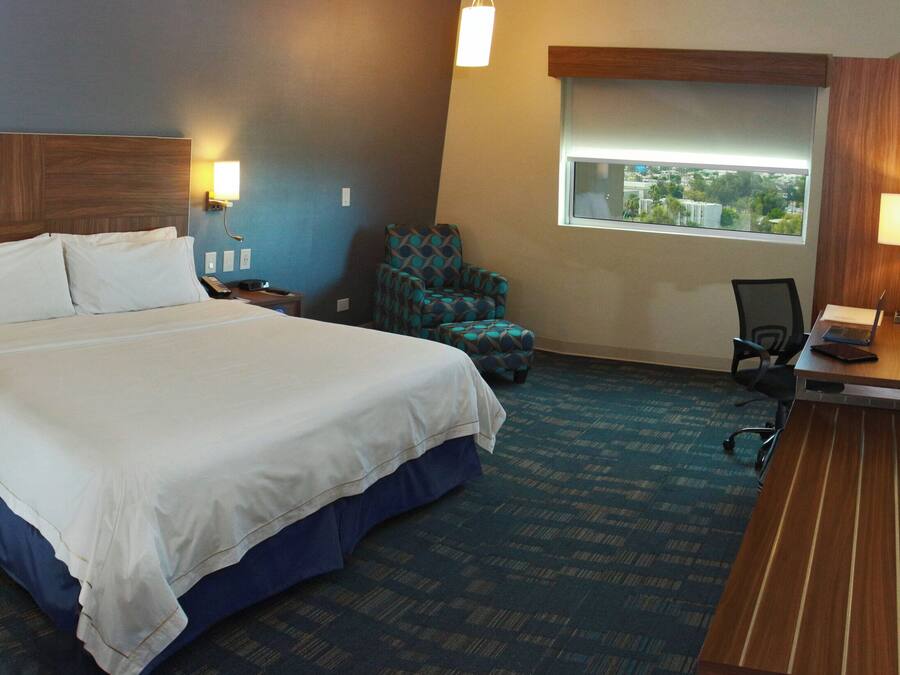 A hotel room with a large bed, a desk with a laptop, a chair, and a window with a view.