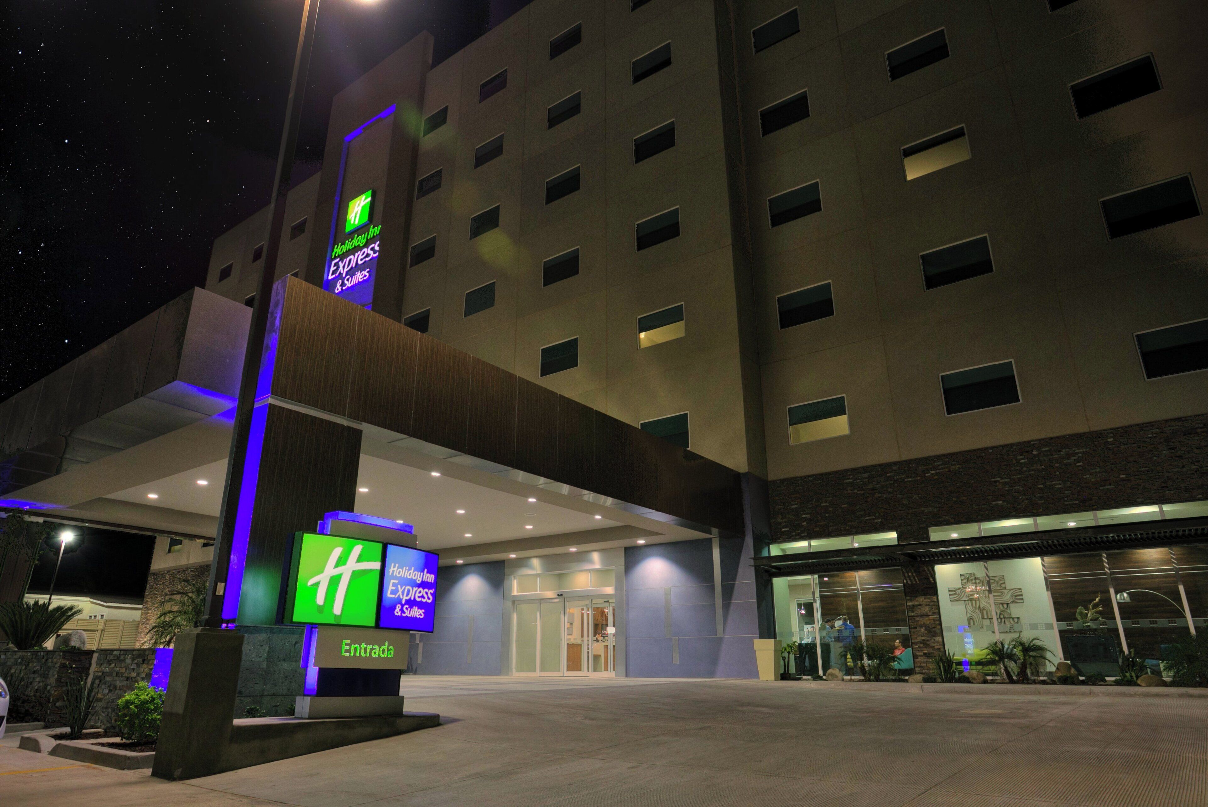Der Eingang eines Holiday Inn Express & Suites Hotels mit modernem Design, erkennbar am großen 'Holiday Inn Express & Suites' Schild und der gut beleuchteten Fassade.