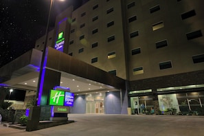 Entrada de un hotel Holiday Inn Express & Suites con diseño moderno, que destaca un cartel prominente de 'Holiday Inn Express & Suites' y una fachada bien iluminada.