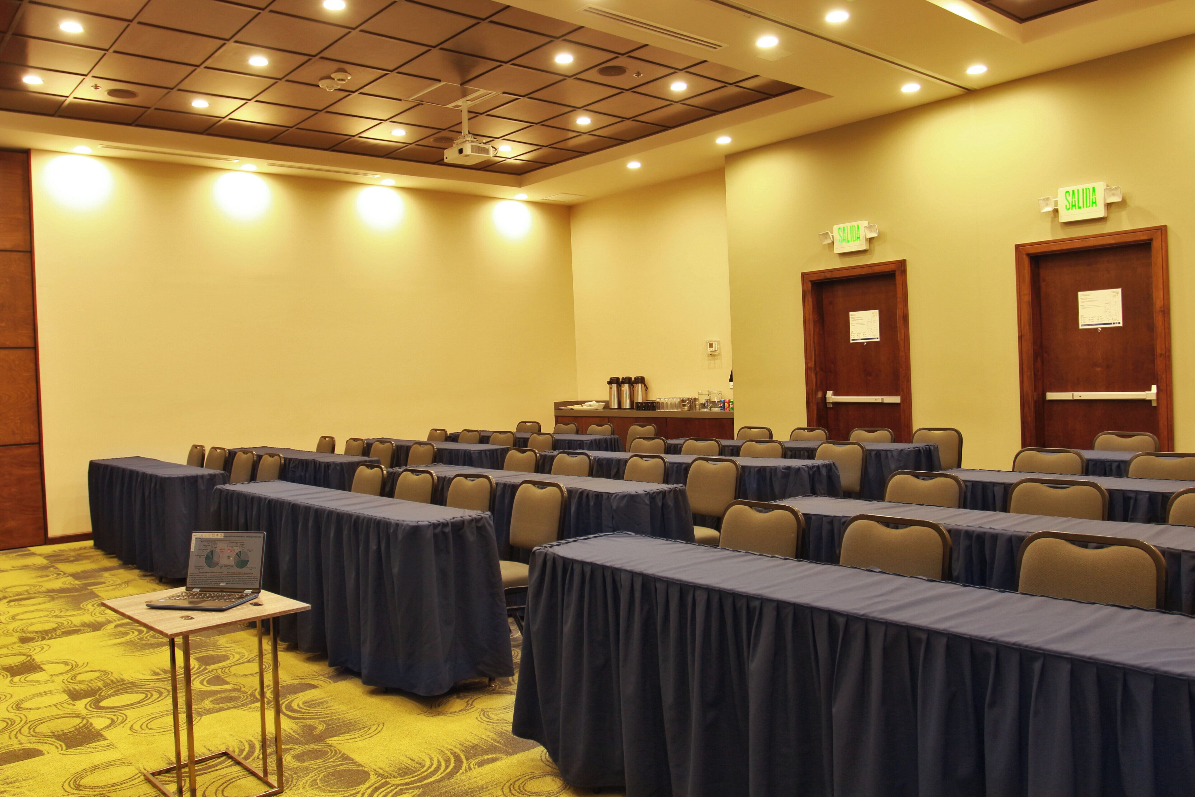 A conference room with rows of tables, chairs, a projector, and a podium.