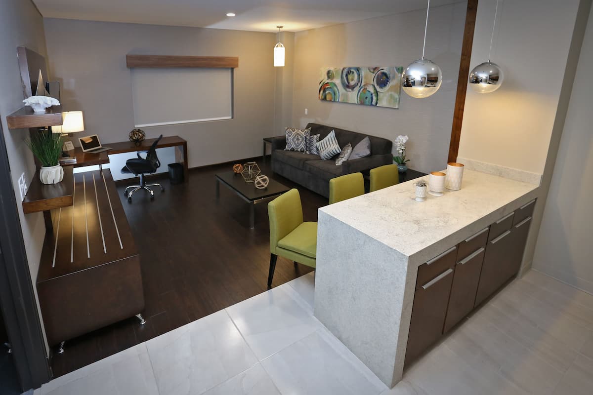 Una cocina moderna con encimera de mármol, un comedor con mesa y sillas, y una sala de estar con sofá y cojines decorativos.