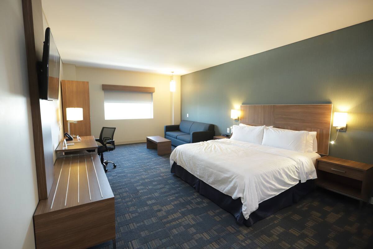 Habitación de hotel con cama, escritorio, silla, sofá y televisor.