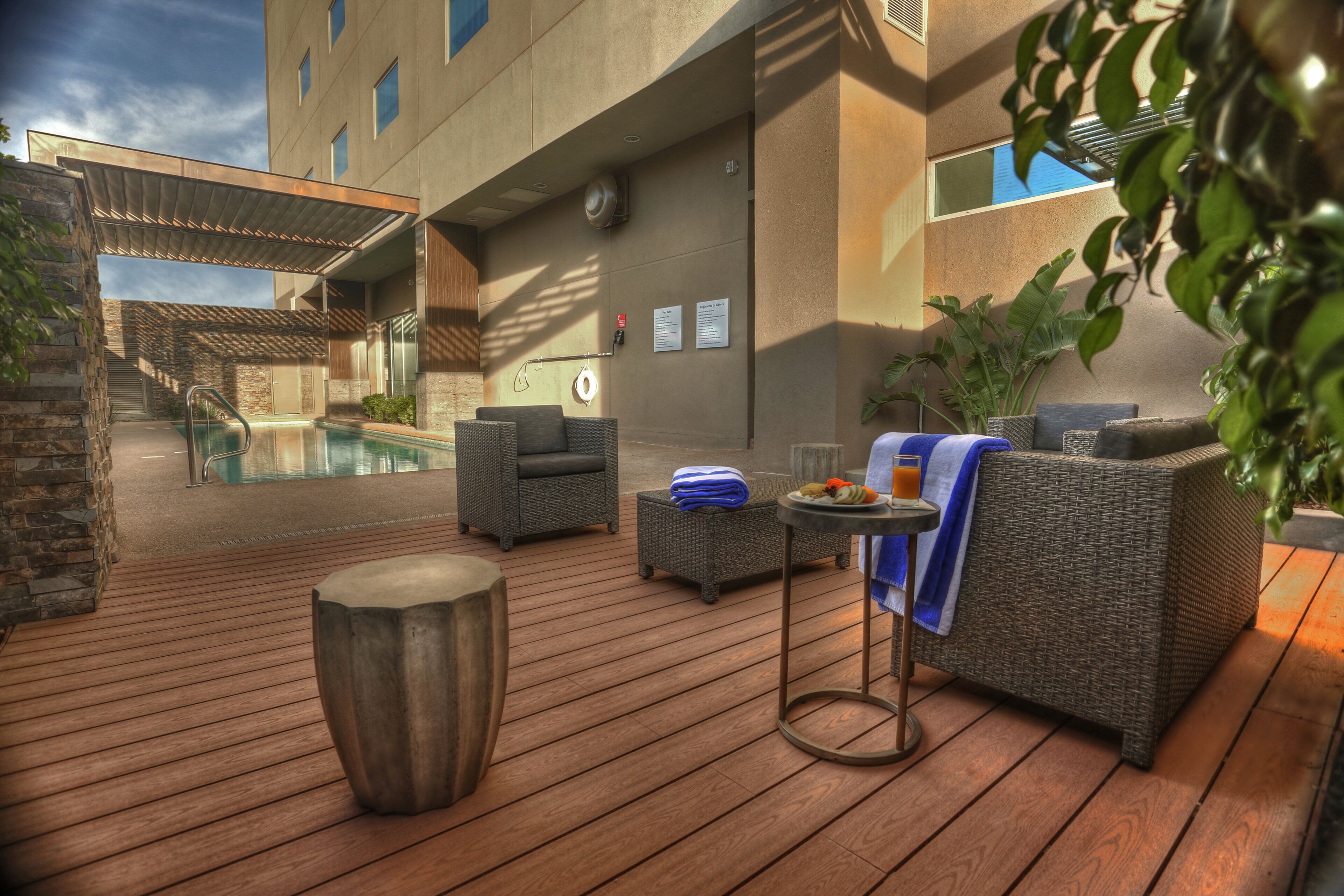 A poolside area with wicker furniture, a small table with a towel, and a wooden stool.