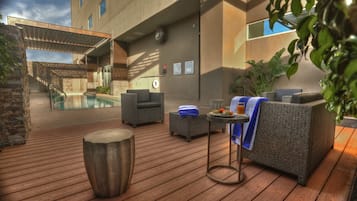 A poolside area with wicker furniture, a small table with a towel, and a wooden stool.
