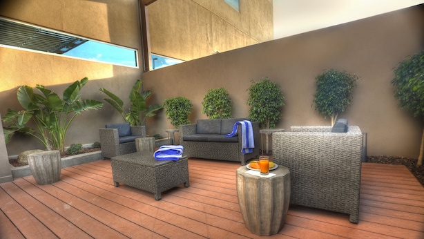 Un área de estar moderna al aire libre con mobiliario de mimbre, plantas en macetas y una terraza de madera.