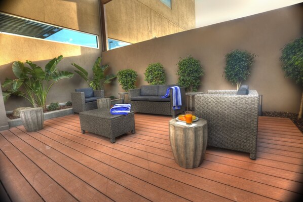 Un área de estar moderna al aire libre con mobiliario de mimbre, plantas en macetas y una terraza de madera.