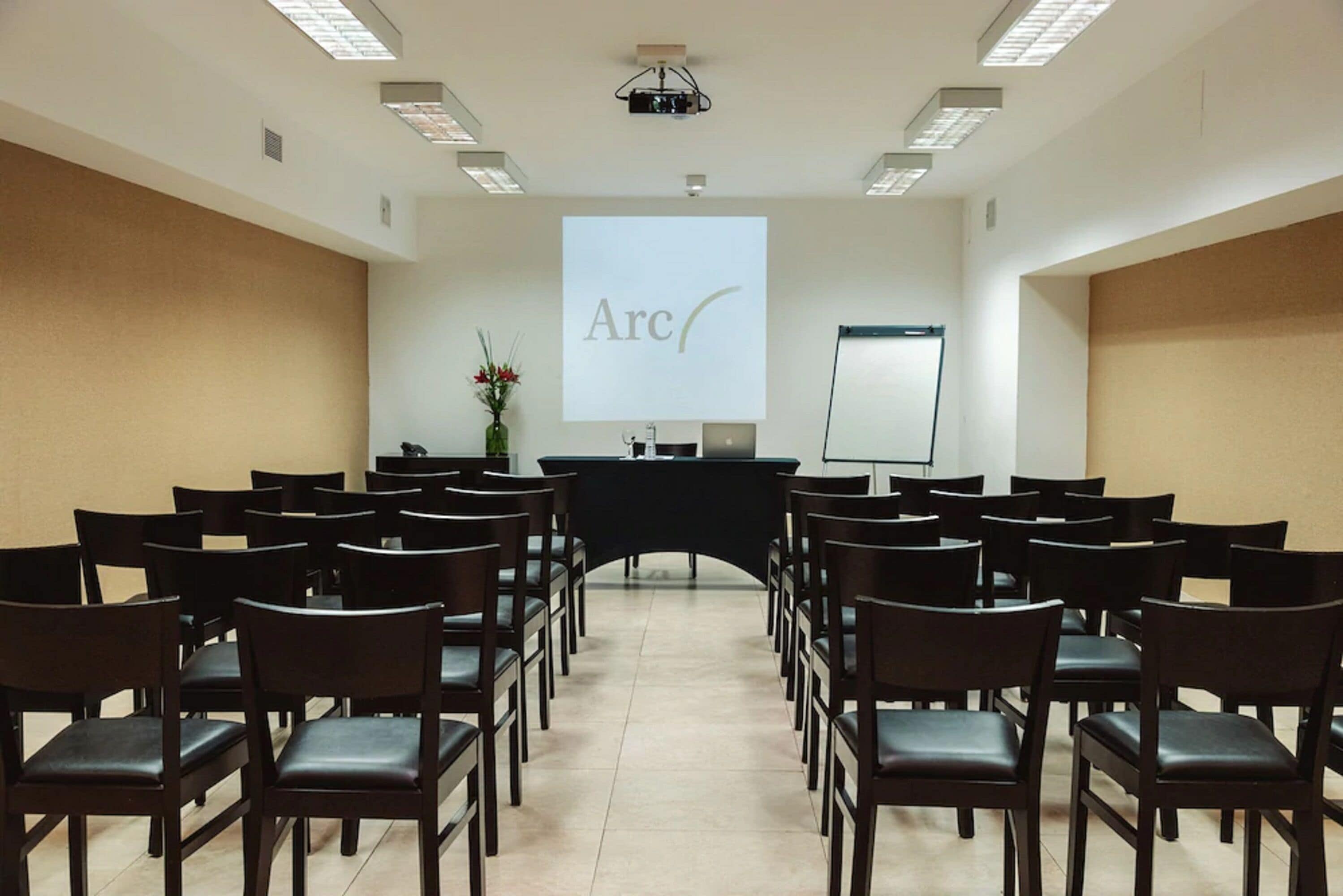 A conference room with rows of chairs facing a projection screen displaying the word "Arc".