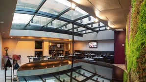 A modern restaurant with a glass ceiling, multiple dining areas, and a green vertical garden.