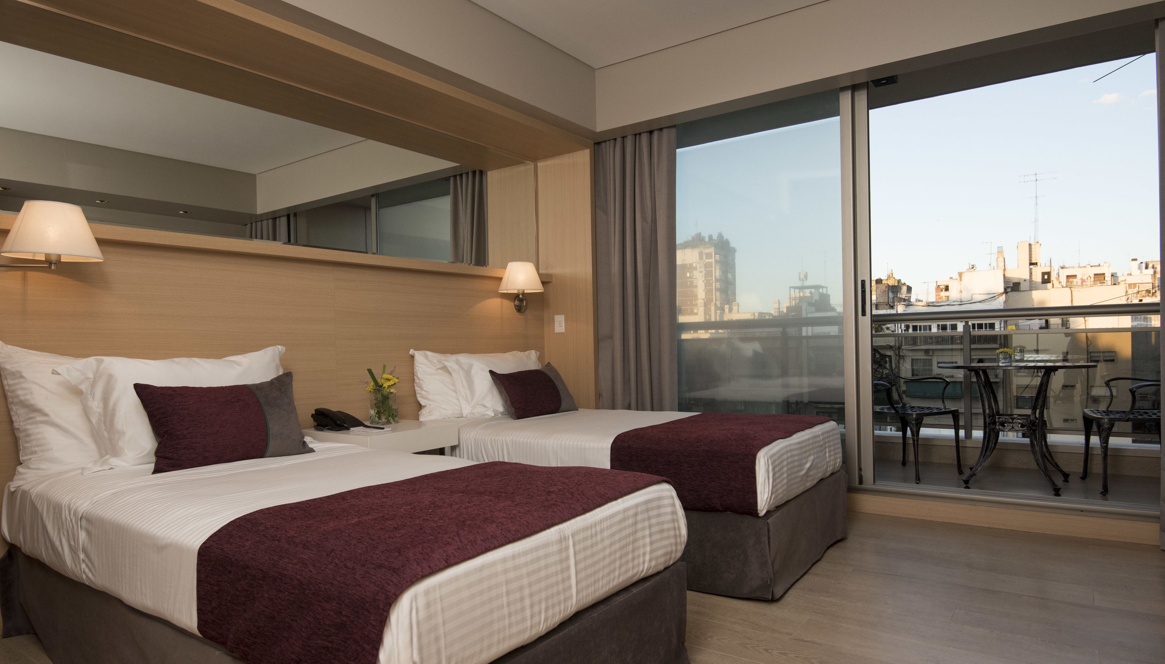 Une chambre d’hôtel avec deux lits, un balcon avec une table et des chaises, et une vue sur la ville.