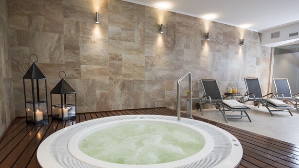 A spa area with a hot tub, lounge chairs, and candles.