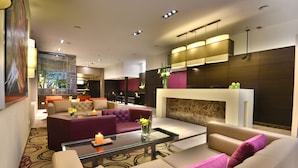 A modern hotel lobby with a seating area, a fireplace, and a large window overlooking the outdoors.