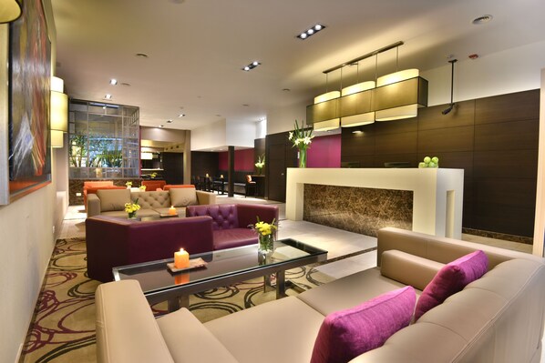 A modern hotel lobby with a seating area, a fireplace, and a large window overlooking the outdoors.