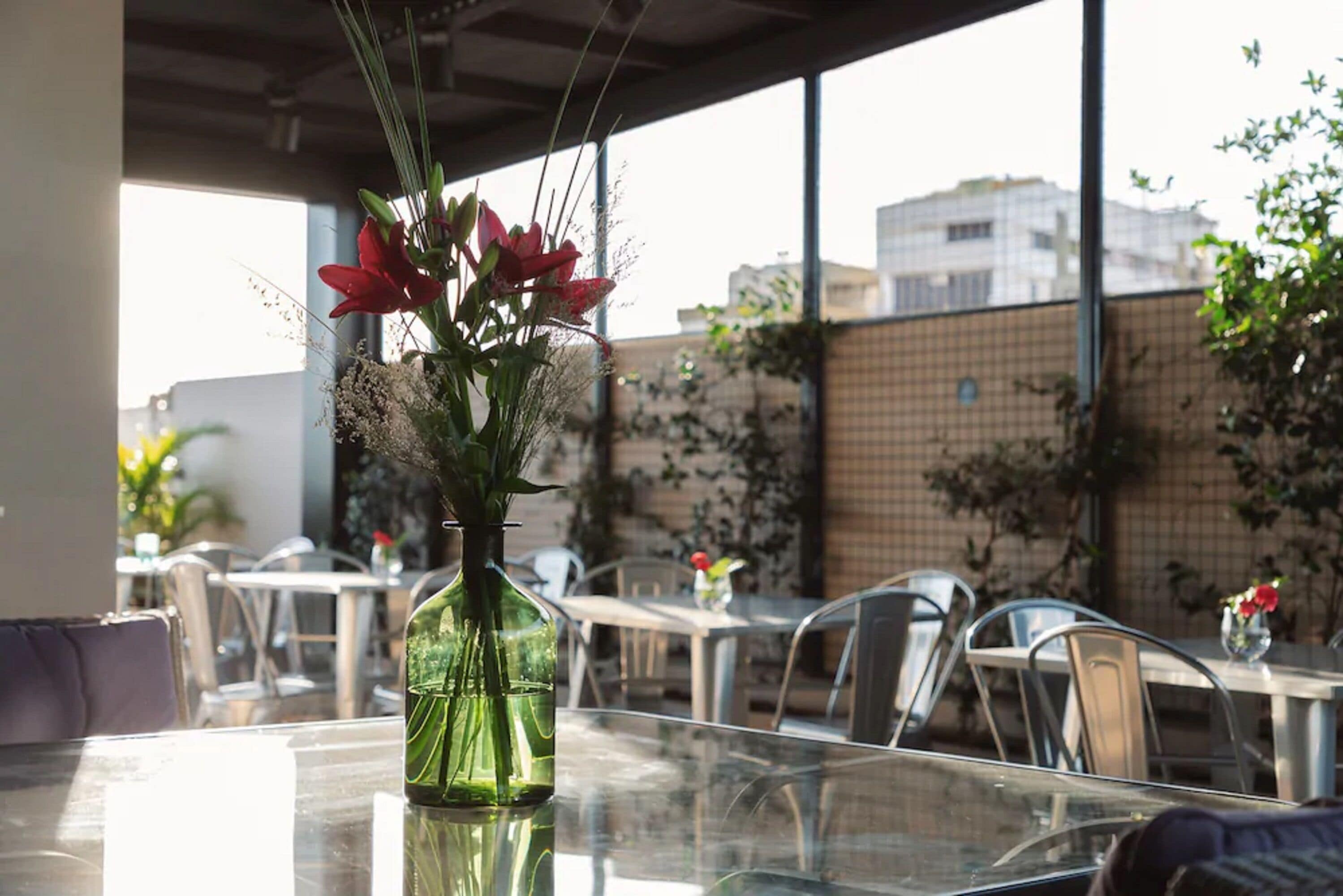 Una mesa de vidrio con un florero verde que contiene flores rojas y follaje.