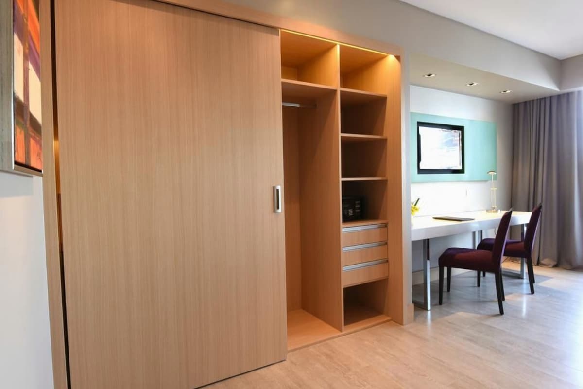 A modern room with a wooden wardrobe, a desk with chairs, and a framed picture on the wall.