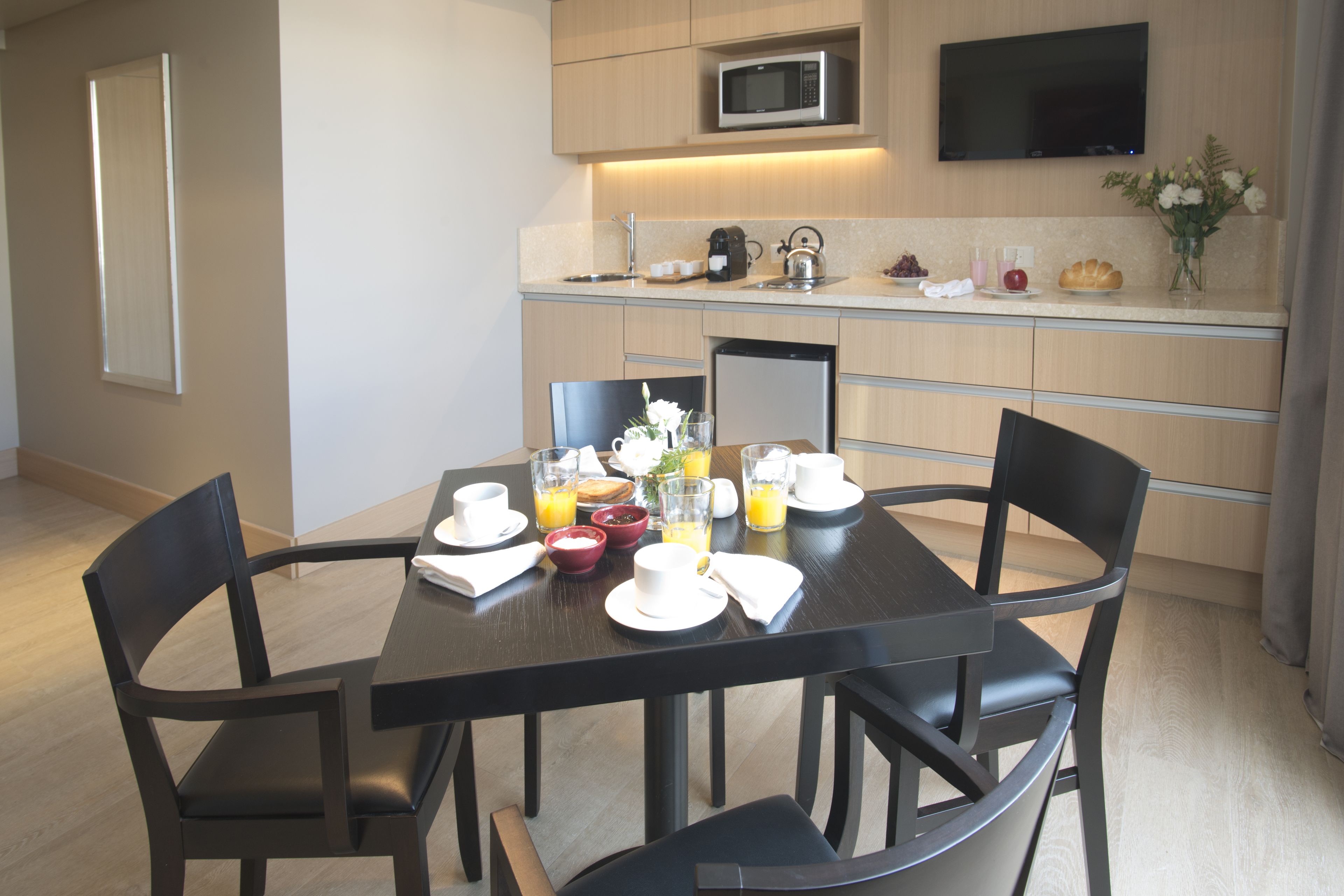 A modern kitchen with a dining table set for breakfast, including plates, cups, and a vase of flowers.
