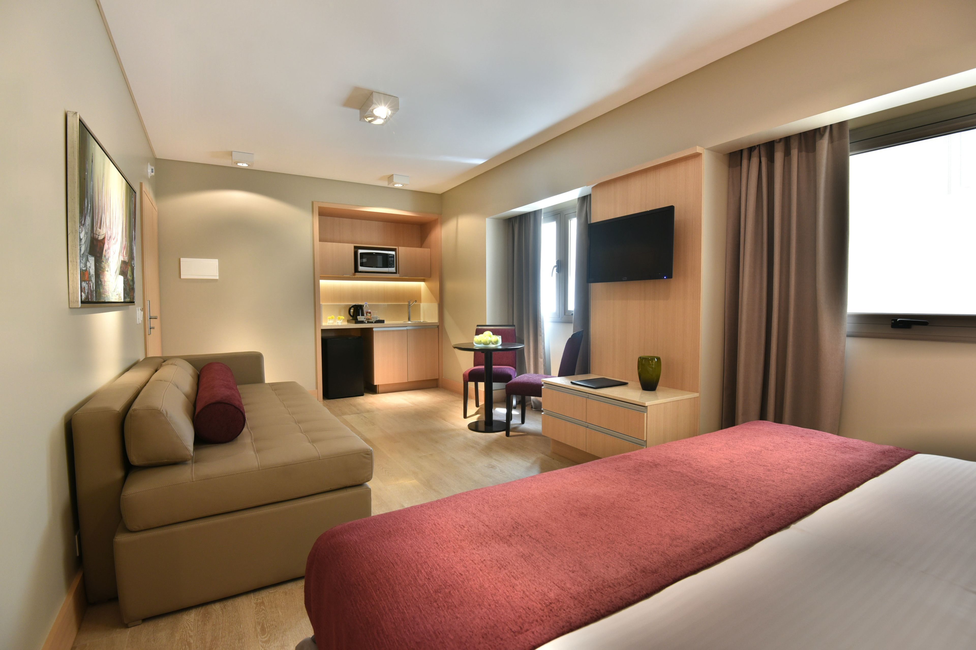 Una habitación de hotel con cama, sofá, escritorio, televisor y kitchenette.