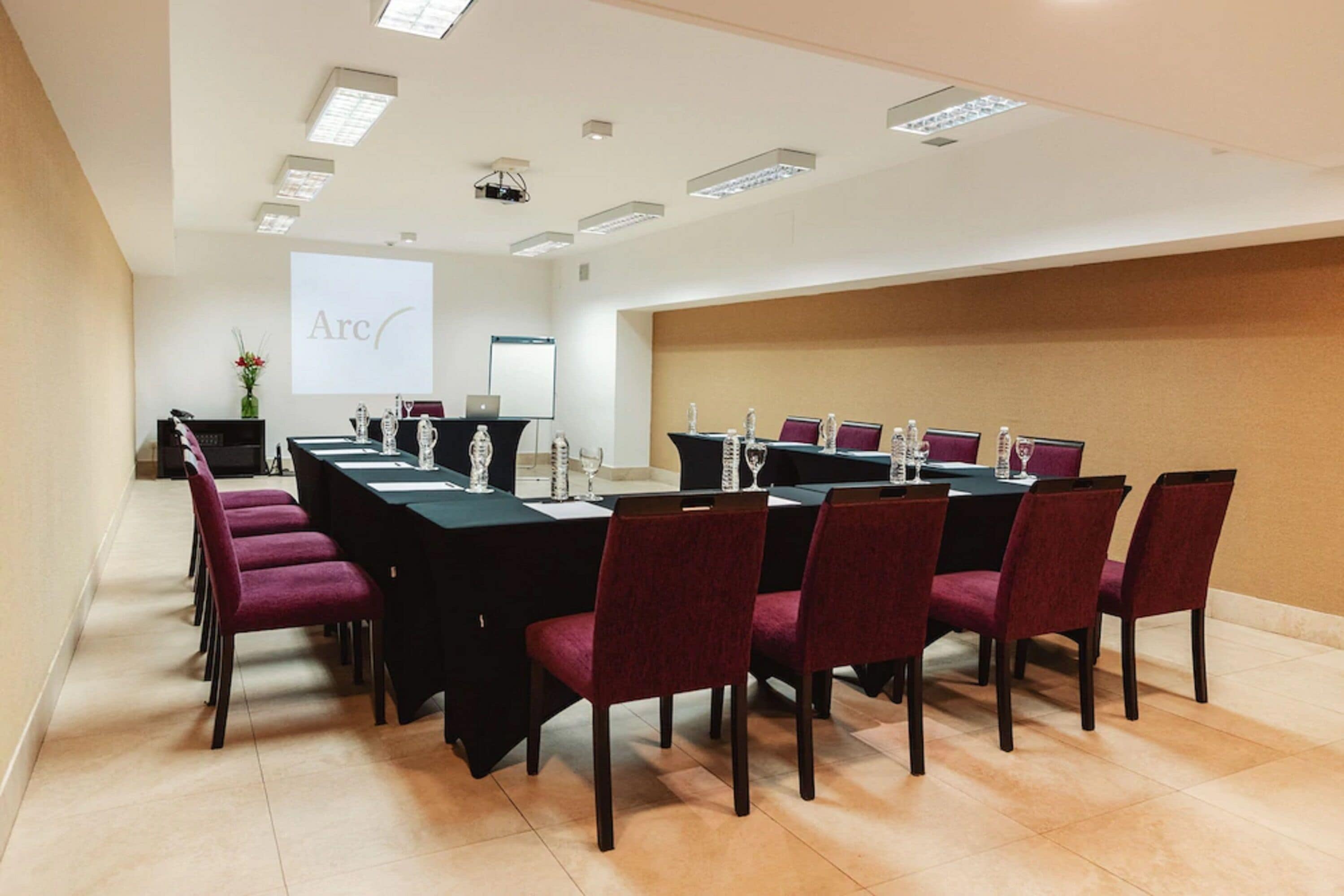 A conference room with a long table, red chairs, and a projector screen displaying "Arc".