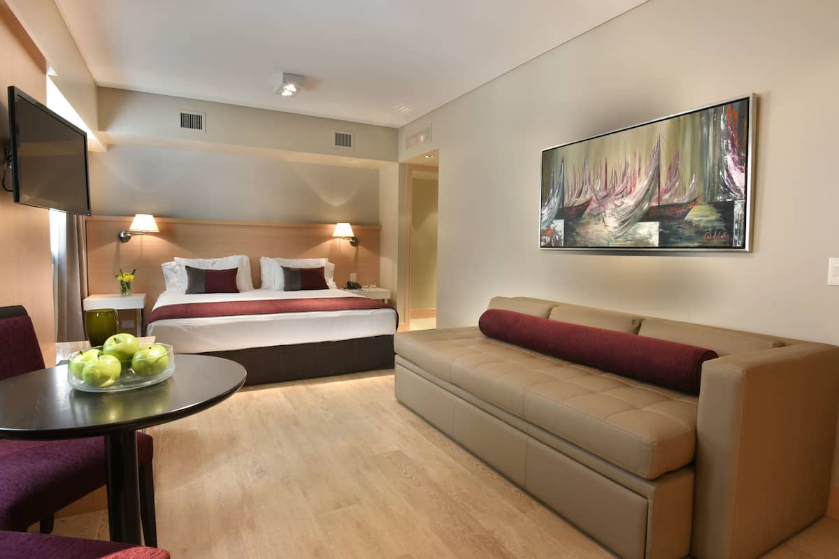 Quarto de hotel com cama, sofá, televisão e um quadro na parede.