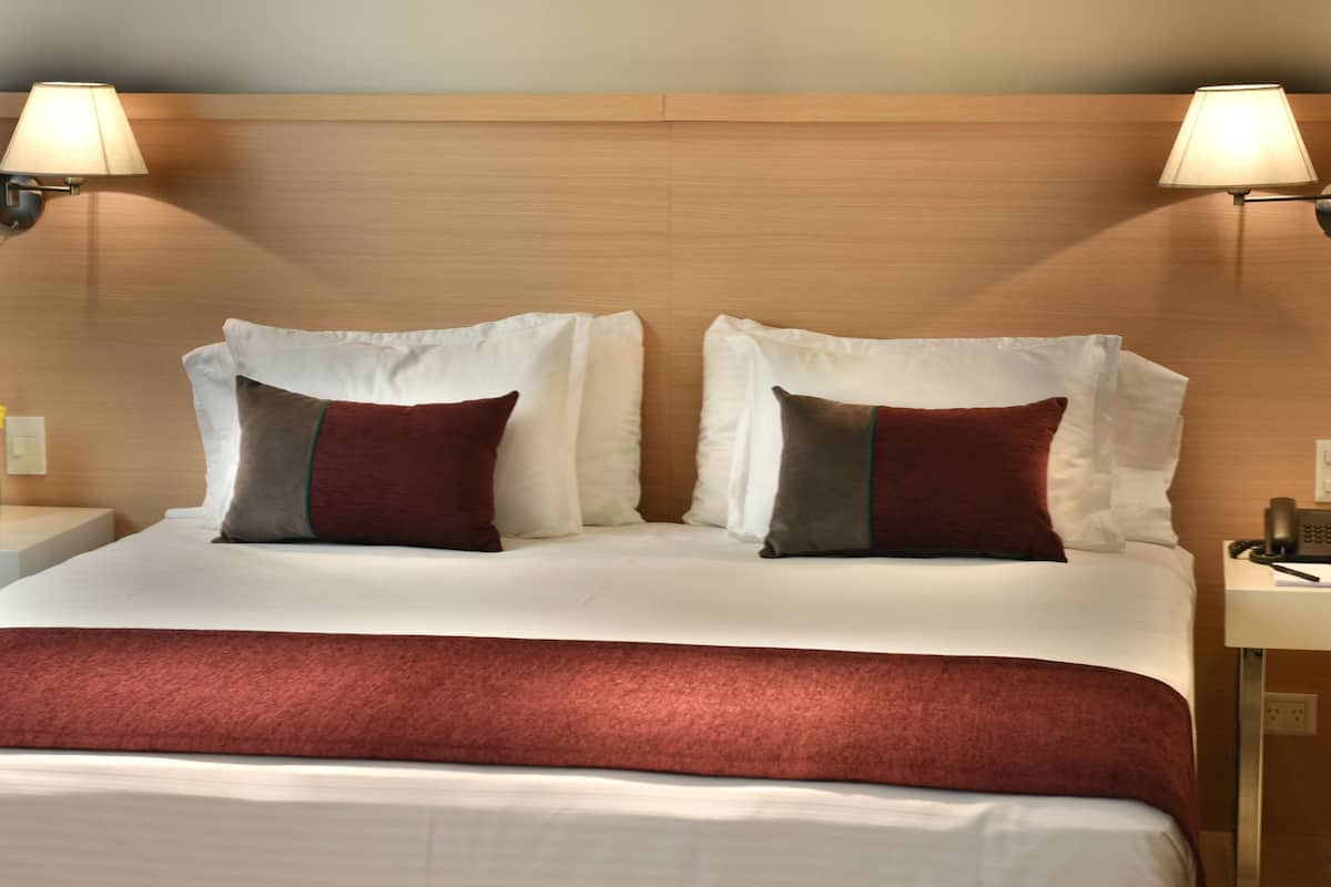Quarto de hotel com uma cama grande, duas luminárias de cabeceira, mesa de cabeceira com telefone e um vaso de flores.