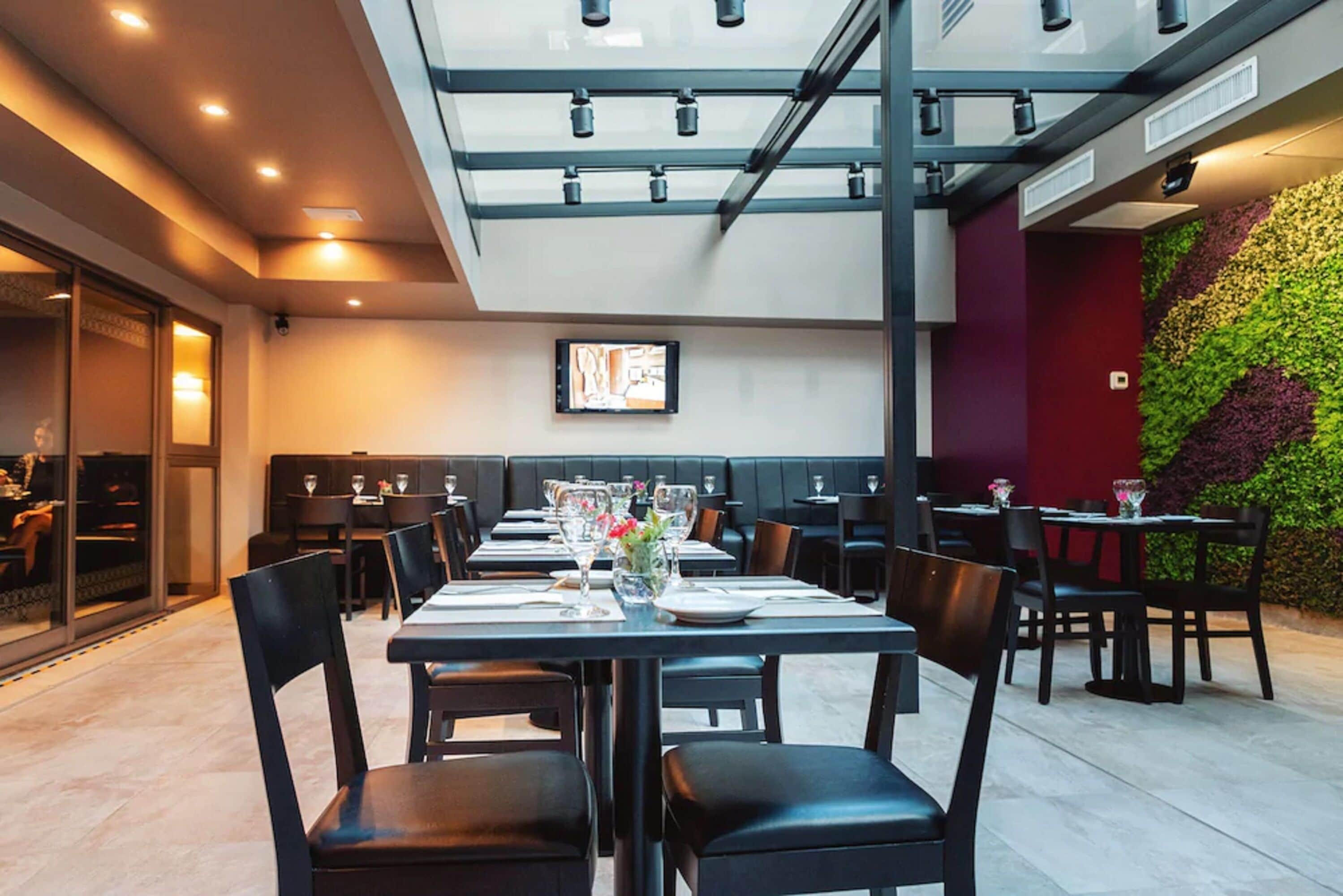 Un restaurante con mesas dispuestas para comer, techo de vidrio y pared verde con plantas.