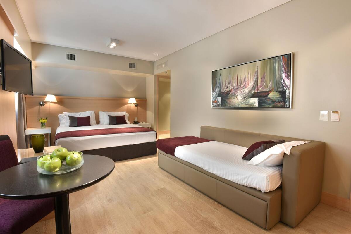 Una habitación de hotel con una cama, un sofá, un televisor y un cuadro en la pared.