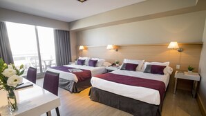 A hotel room with two beds, a dining table, and a view of the city.