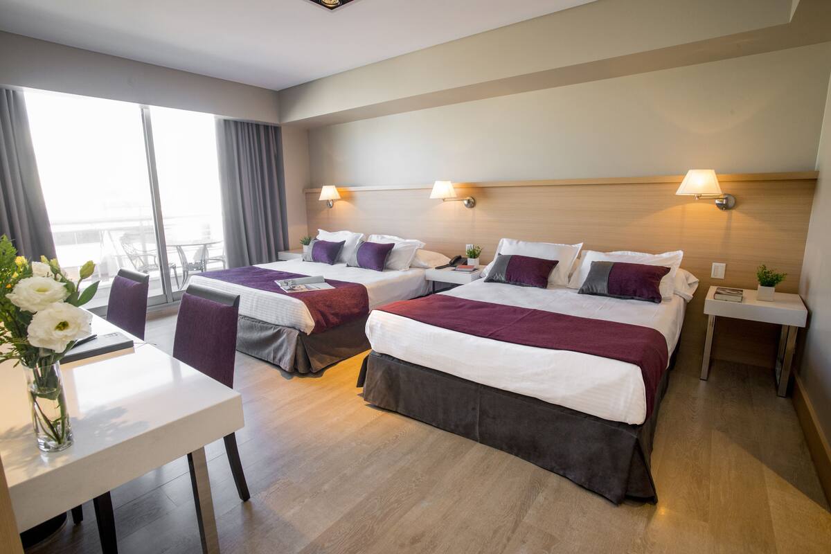 Quarto de hotel com duas camas, uma mesa de jantar e vista para a cidade.