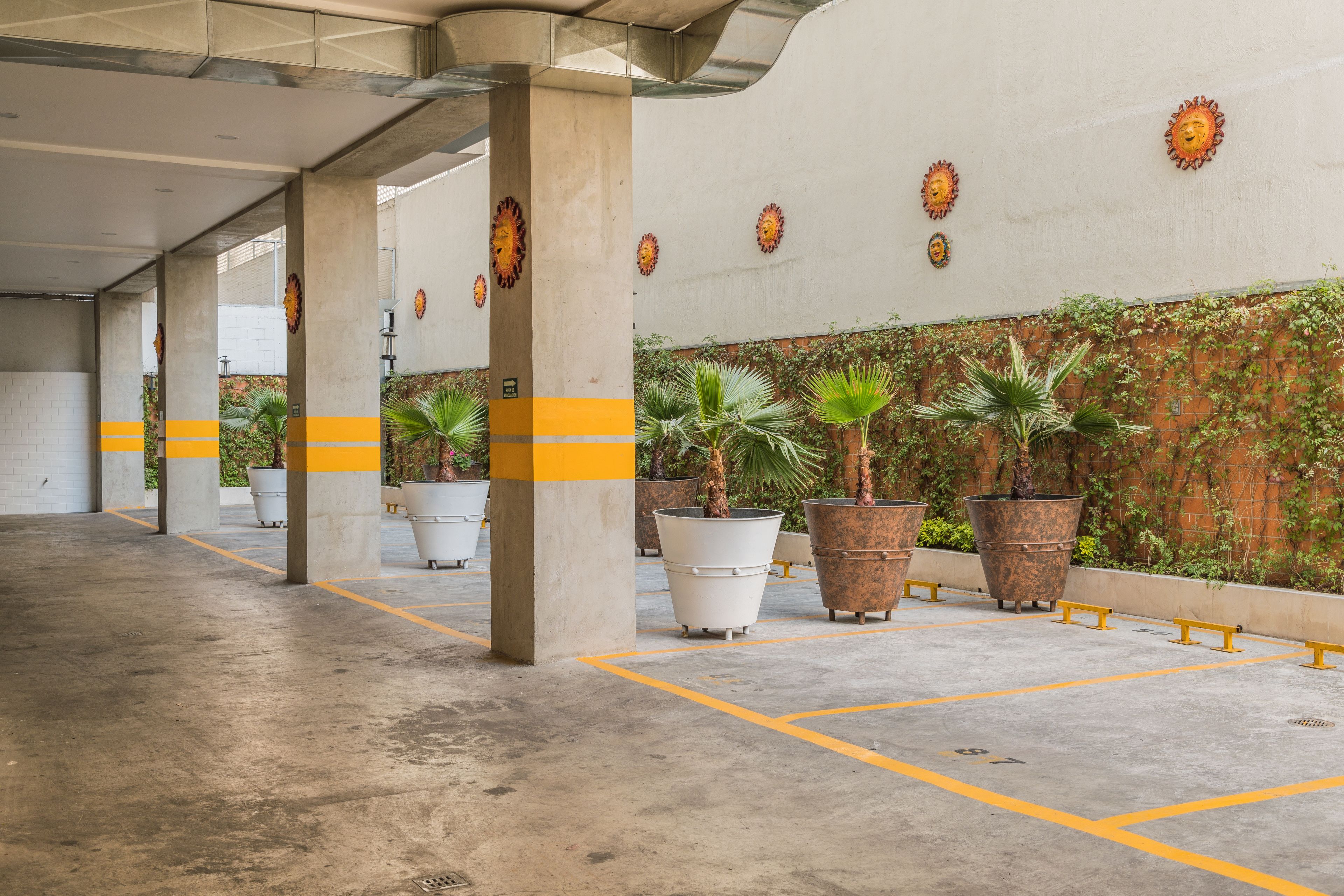 A covered parking area with concrete pillars, yellow lines, and potted plants.