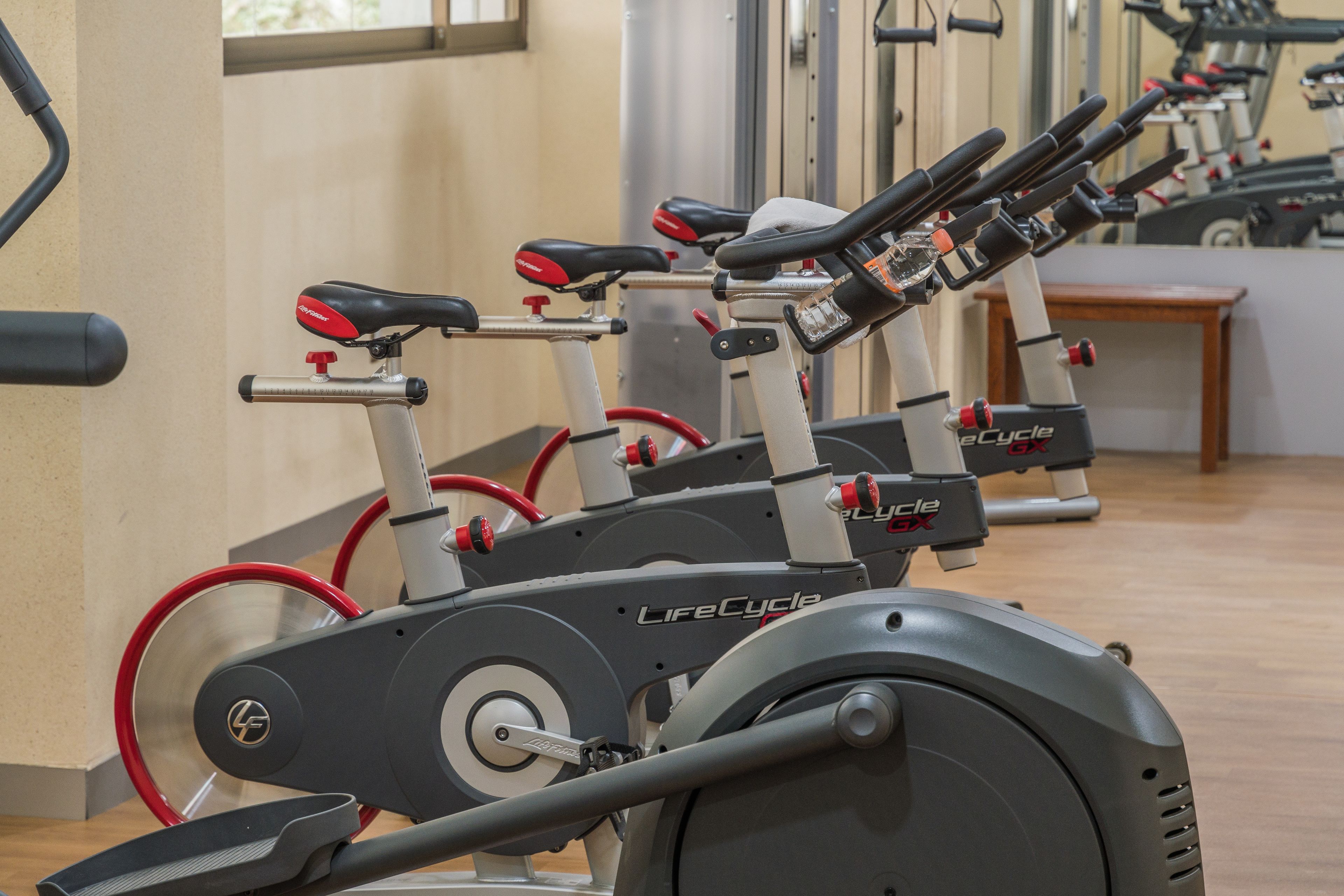 A row of stationary bikes in a gym with mirrors on the wall.