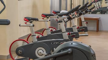 A row of stationary bikes in a gym with mirrors on the wall.