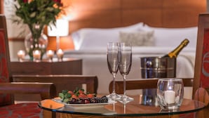 A dining table with a plate of fruit, two glasses, a candle, and a champagne bottle.