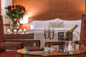 A dining table with a plate of fruit, two glasses, a candle, and a champagne bottle.