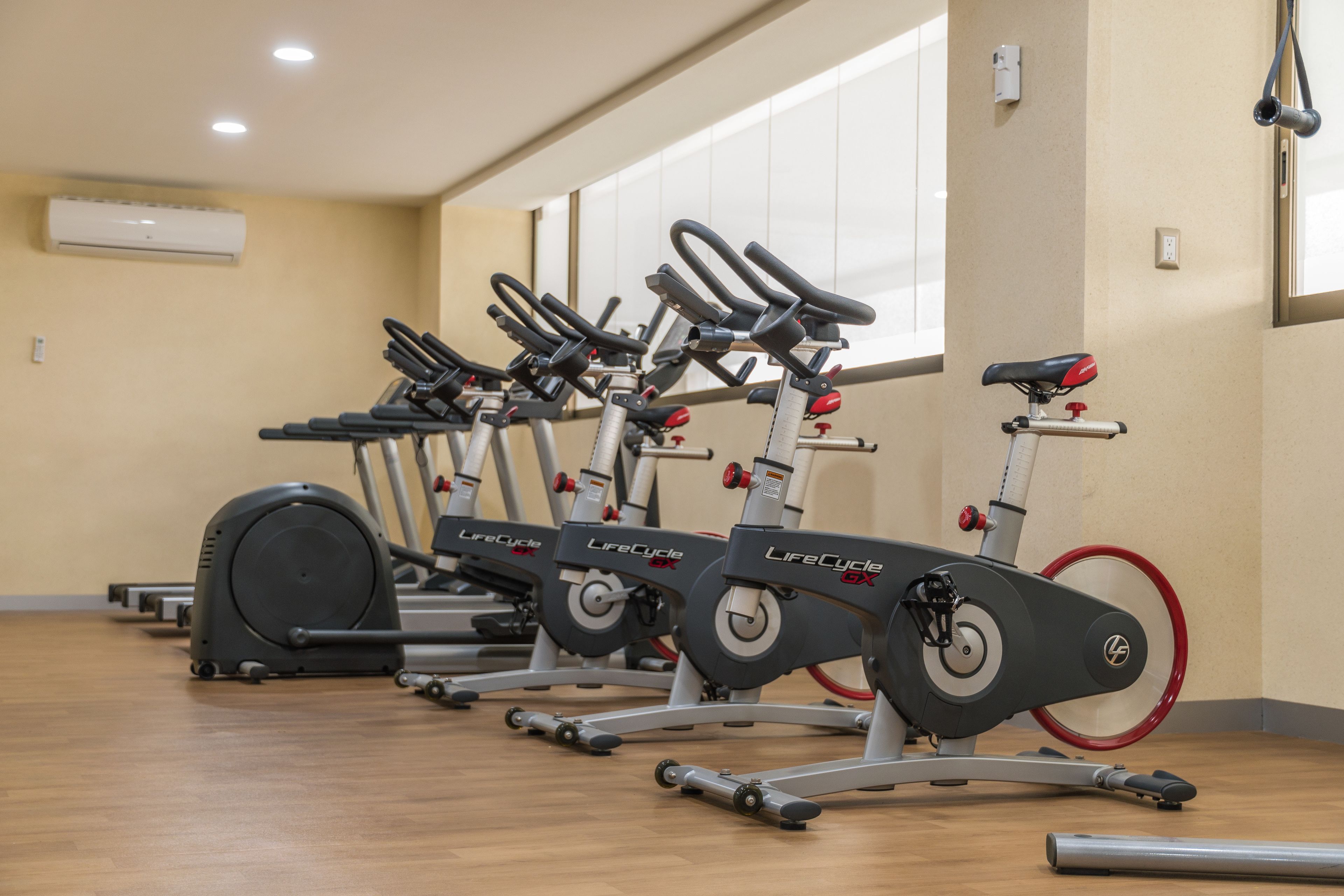 A row of stationary bikes in a gym with wooden flooring and beige walls.